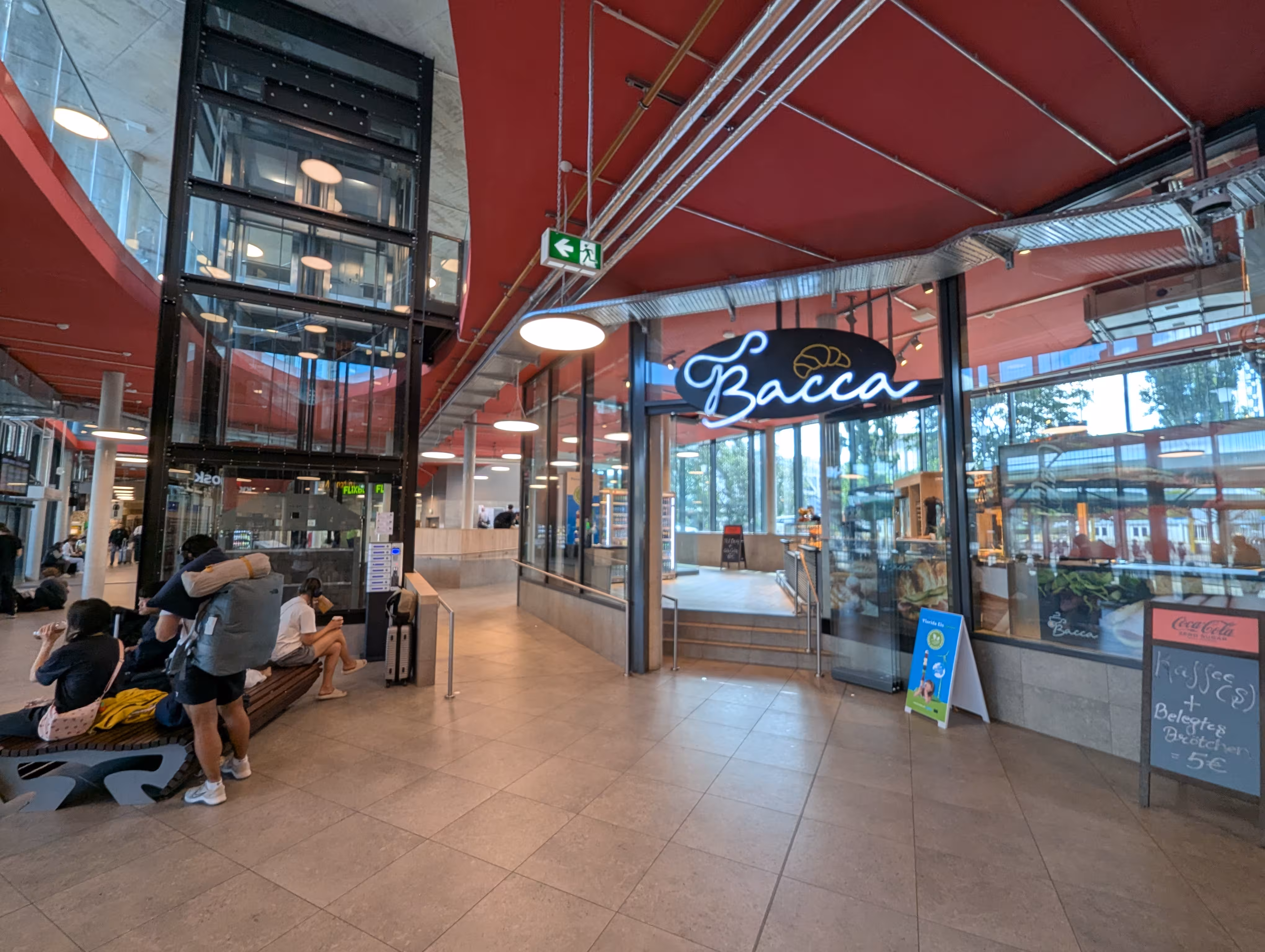 Das Zentrum der Wartehalle mit einem Aufzug links und dem Backwarengeschäft Bacca rechts