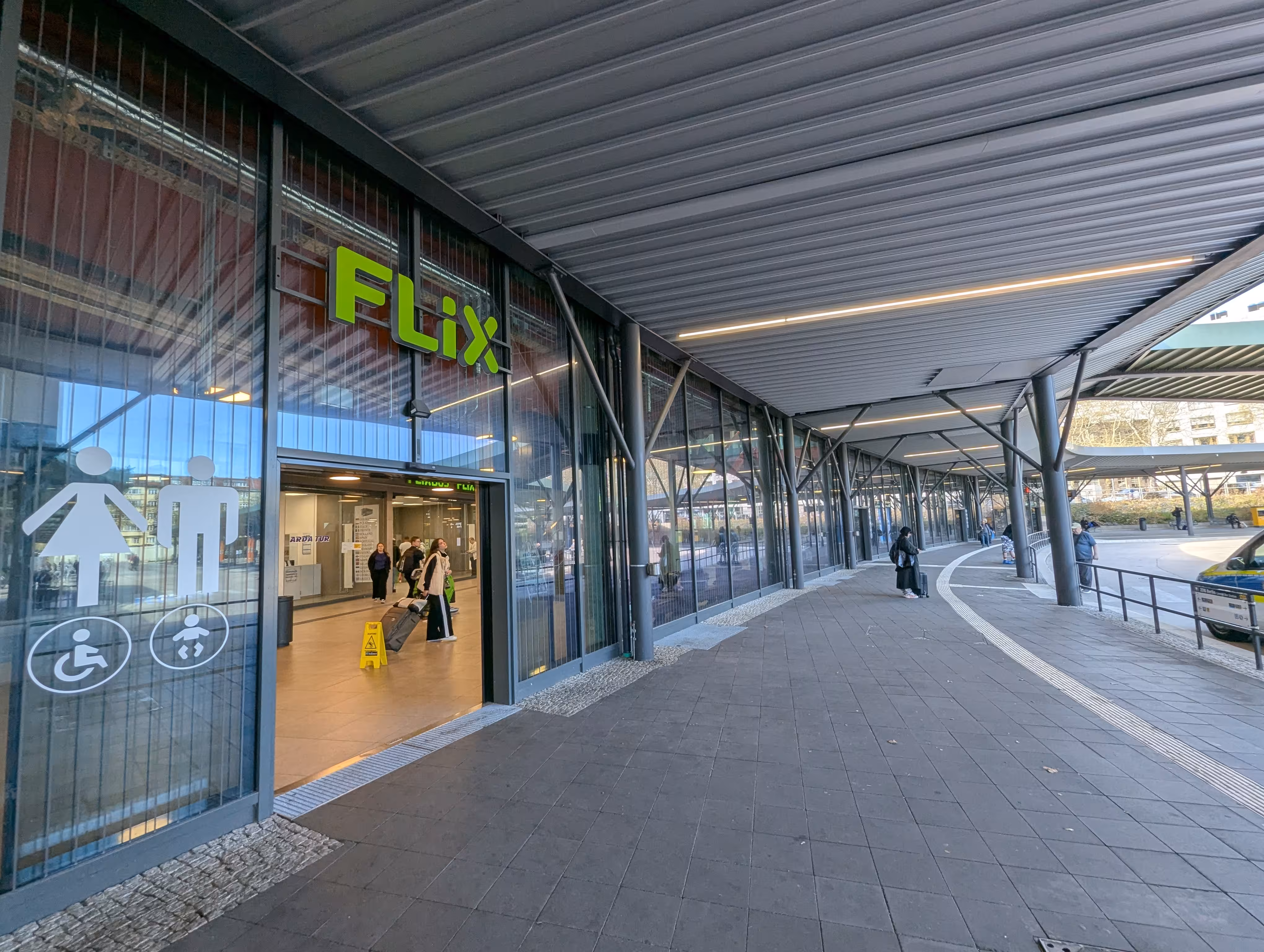 Ein Eingang zur Wartehalle, über ihm hängt ein Flix-Logo, neben der Tür ist zudem ein Piktogramm für die Toiletten angebracht